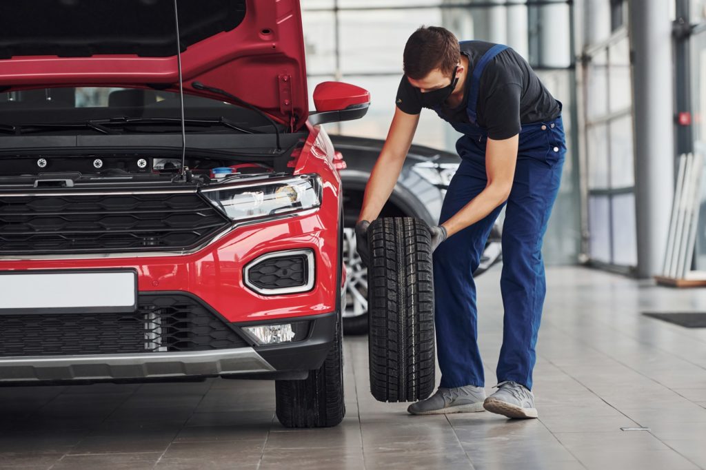 Man in uniform changing tire of automobile. Conception of car service